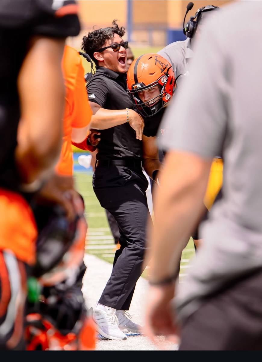 Kelvin celebrating a play on the sideline with a helmeted football player.