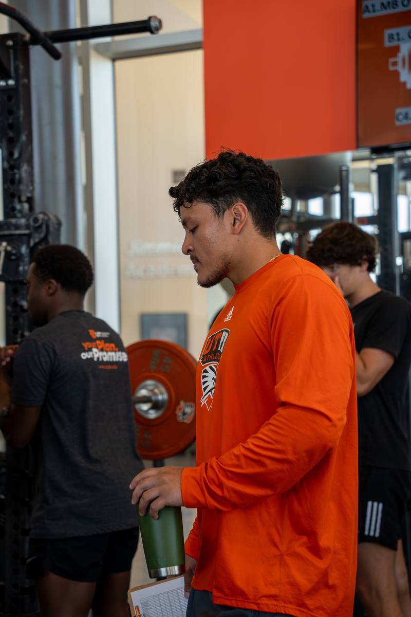 Kelvin with a clipboard on the weight room floor at UTPB.