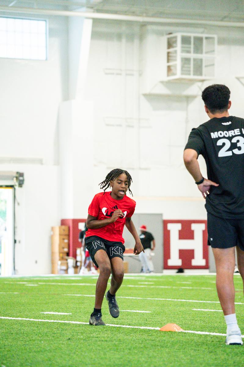 A young athlete sprinting through a cone drill in an indoor facility while Kelvin coaches.